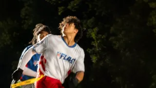 Two men running while looking behind them to watch the football while its in the air.