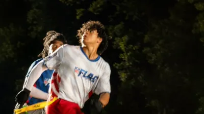 Two men running while looking behind them to watch the football while its in the air.