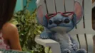 Stitch looks at Lilo while relaxing on a white chair with red sunshades on his head and his right arm on the arm rest.