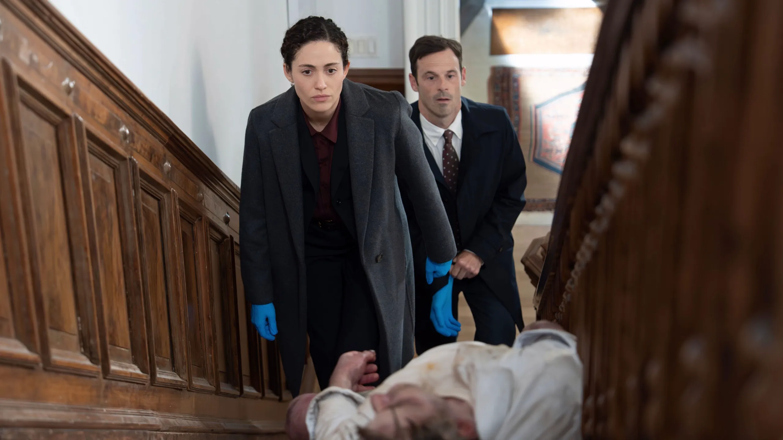 Alice and Danny examine a body on a staircase.