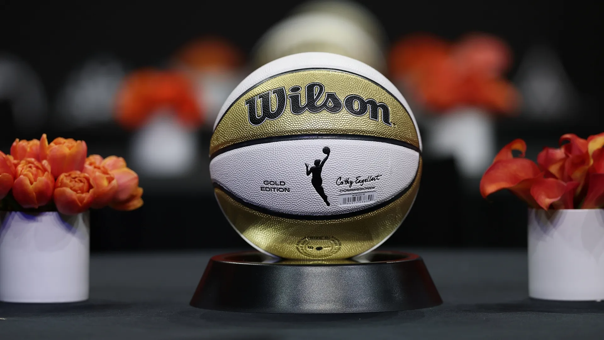 A Gold Edition WNBA basketball sits on a display stand surrounded by flowers.