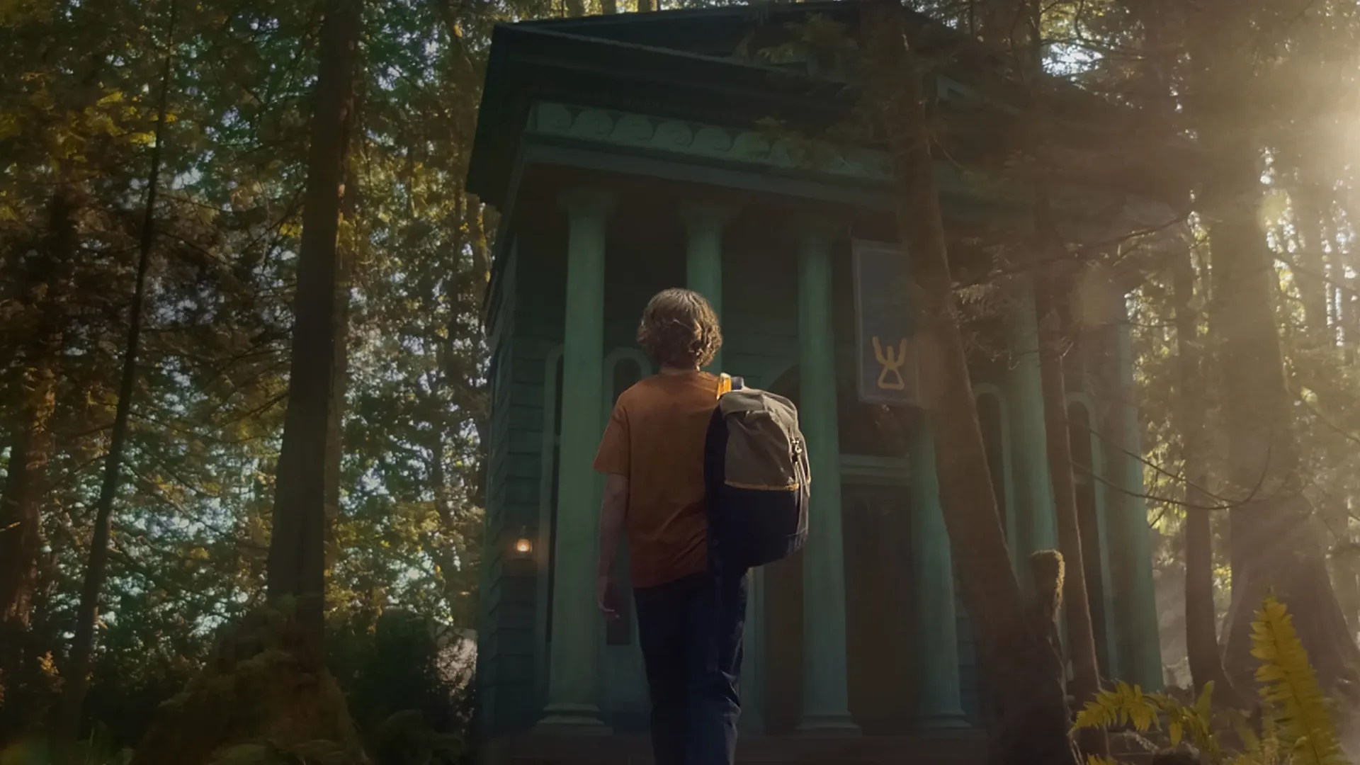 Percy Jackson (Walker Scobell) approaches a large structure in a forest.