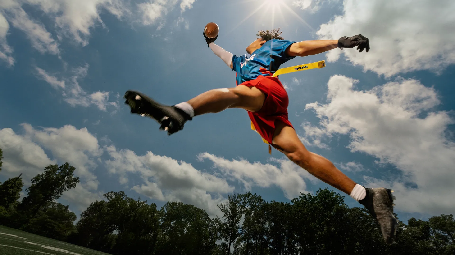 A young man playing flag football reaches for the ball in the air.