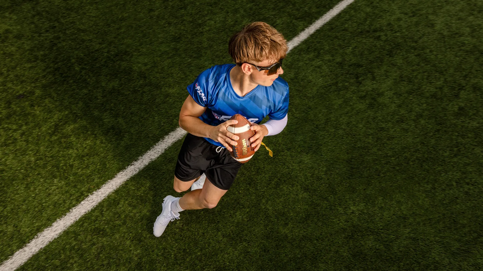 Overhead close-up of a young man running with the ball in a game of flag football.