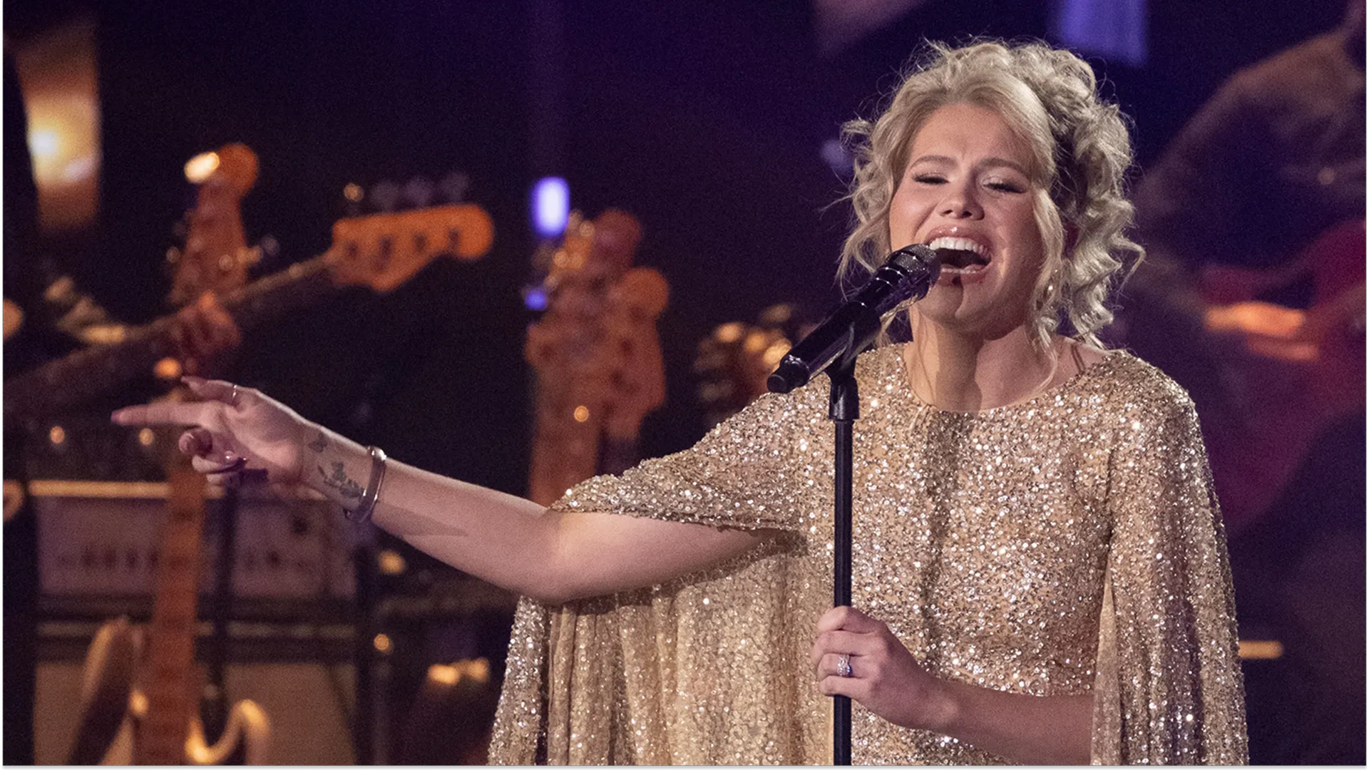 Closeup of American Idol finalist Hannah Harper singing on stage, in a sequinned gold dress with a cape