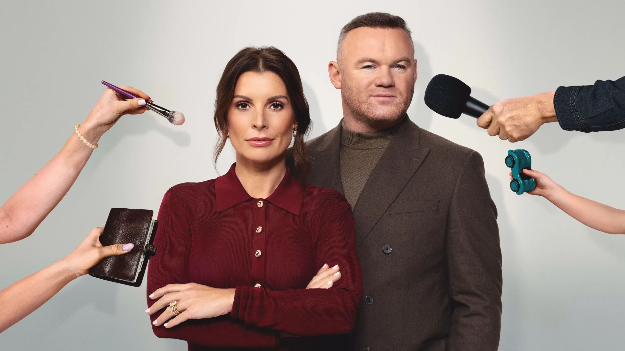 Wayne Rooney and Coleen Rooney pose together as hands hold a microphone, makeup brush, notebook and toy car in The Real Rooneys.