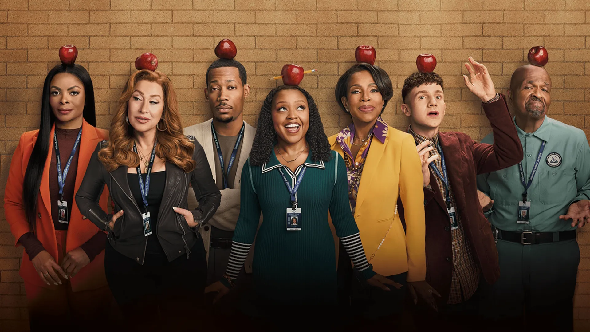The cast of Abbott Elementary stand in front of a brick wall with red apples balanced on their heads