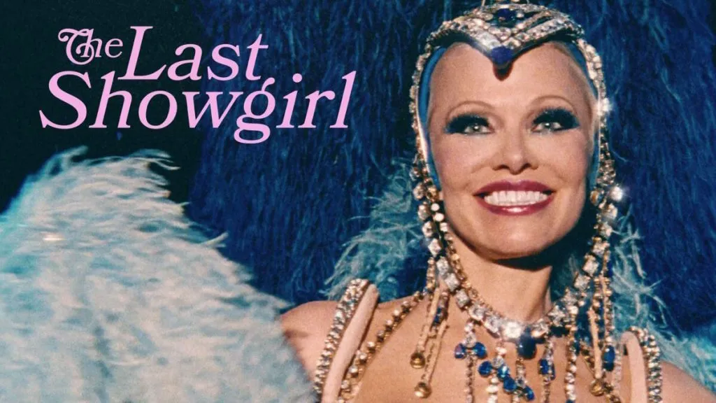 Title art for The Last Showgirl featuring a smiling performer in an elaborate blue feathered headdress and bejeweled costume under stage lights.