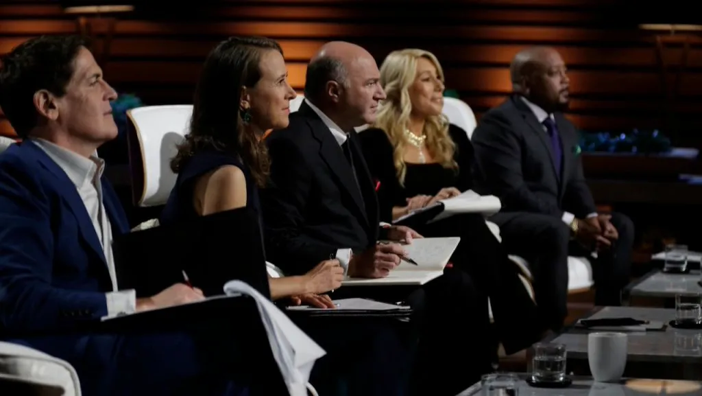 The panel of investors from Shark Tank sitting in their chairs, attentively listening to an entrepreneur’s pitch in the studio.