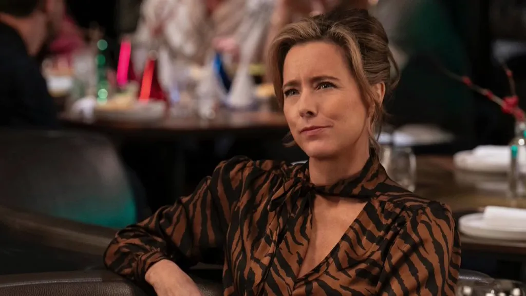 Téa Leoni sits in a restaurant wearing a brown and black patterned blouse.