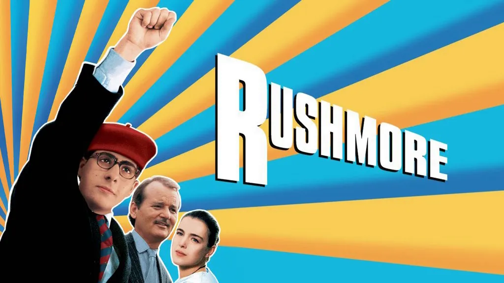 Jason Schwartzman as Max Fischer in Rushmore, raising his fist triumphantly with Bill Murray and Olivia Williams behind him.