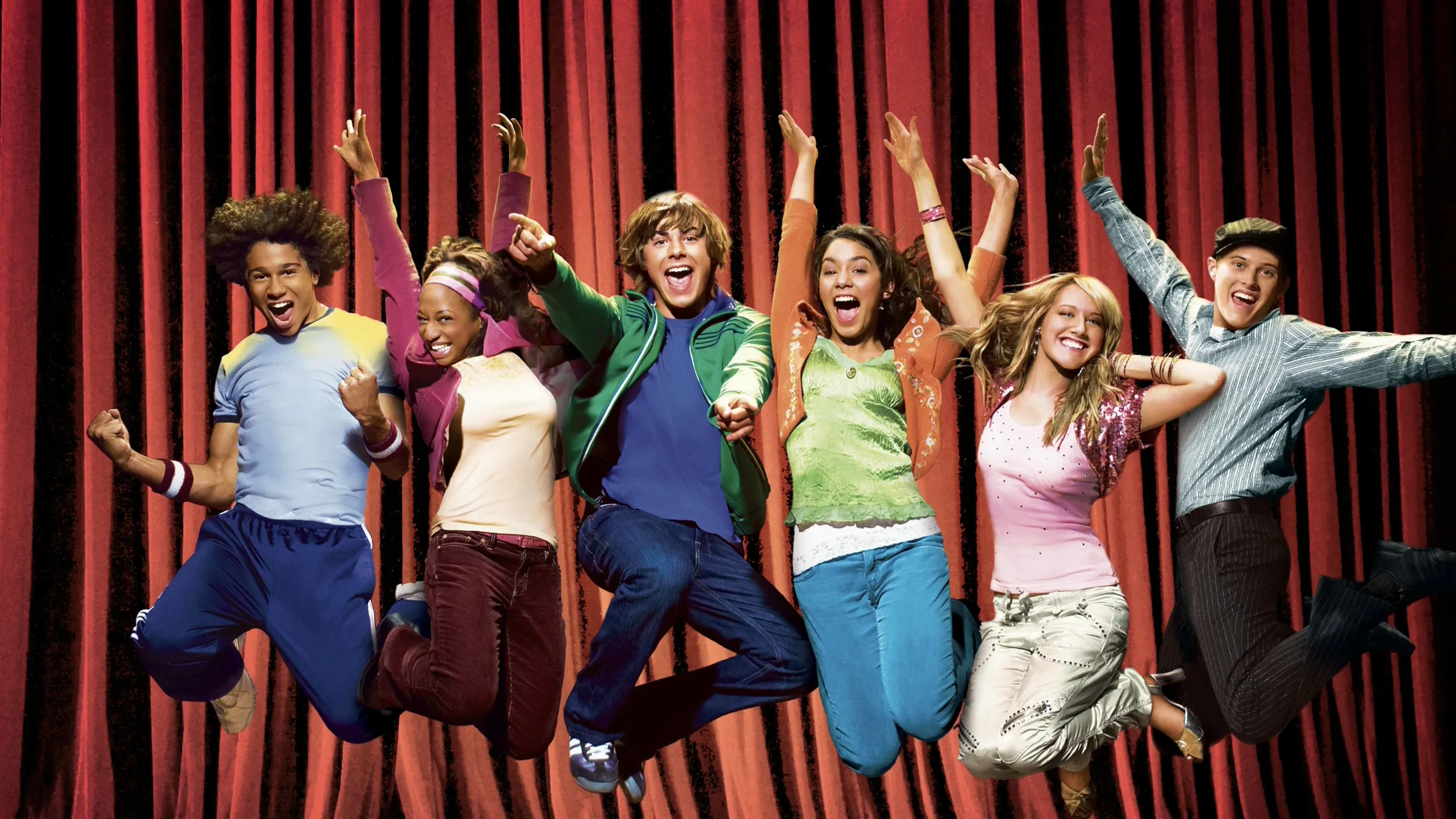 The cast of Disney’s High School Musical jumping in the air in front of a red theater curtain.