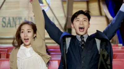 A man and woman raise their arms in celebration in a scene from the Korean drama What’s Wrong With Secretary Kim.