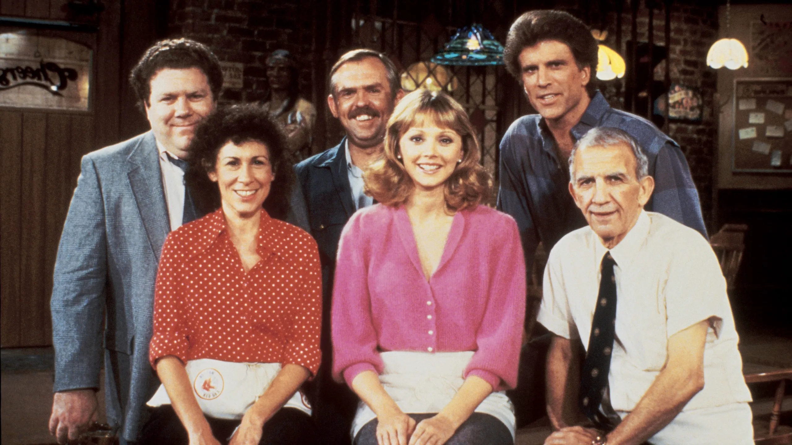 The cast of the 1980s sitcom Cheers posing together inside the show’s bar.