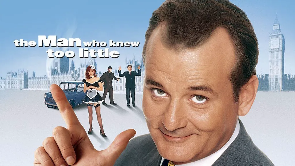 Bill Murray as Wallace Ritchie in The Man Who Knew Too Little, smiling mischievously and pointing in front of a London city backdrop.