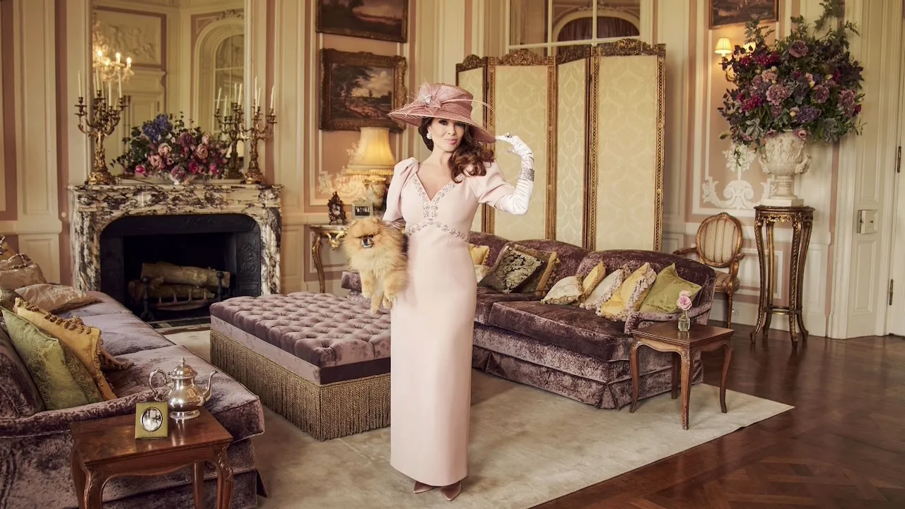 Lisa Vanderpump dressed in a pink dress and hat, holding a small dog in a luxurious villa living room.