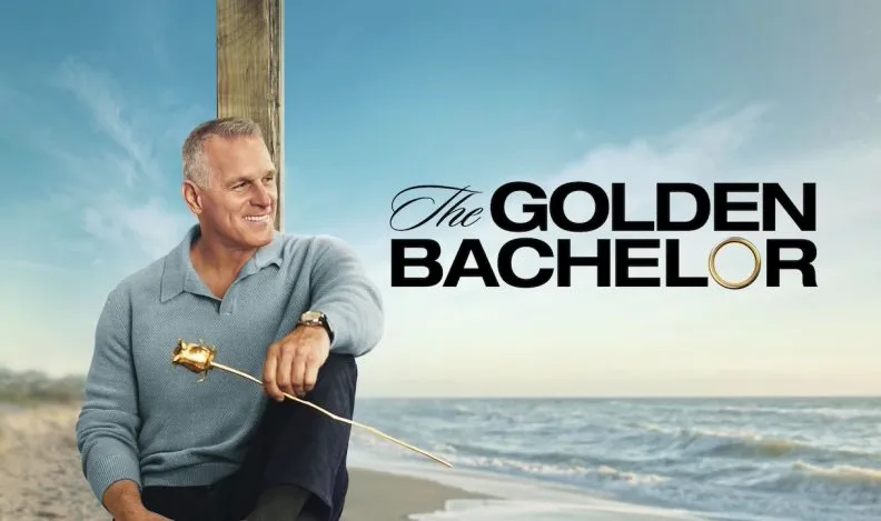A smiling man holding a golden rose sits by the beach with ocean waves behind him, alongside the title text ‘The Golden Bachelor.’