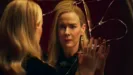 An elegant blonde woman, Cordelia Goode (Sarah Paulson), stares with a distressed and emotional expression at her reflection in a severely shattered mirror, her hand pressed flat against the cracked glass.